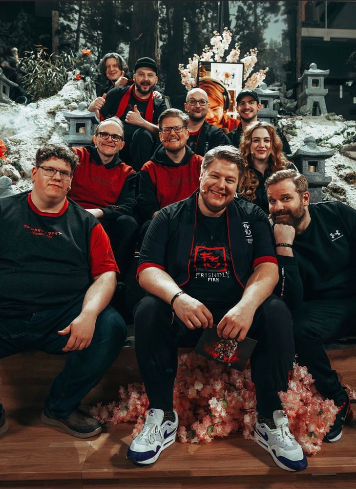Alle Talents von Friendly Fire sitzen untereinander auf der Treppe der Hauptbühne, tragen den Merch und freuen sich und lachen in die Kamera. Der Hintergrund ist japanisch gestaltet!