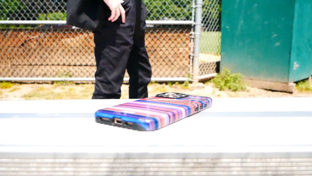 A phone is laying face down on bleachers in a park, and in the distance is The Last Doctor (Iris Prindel), in a messy suit