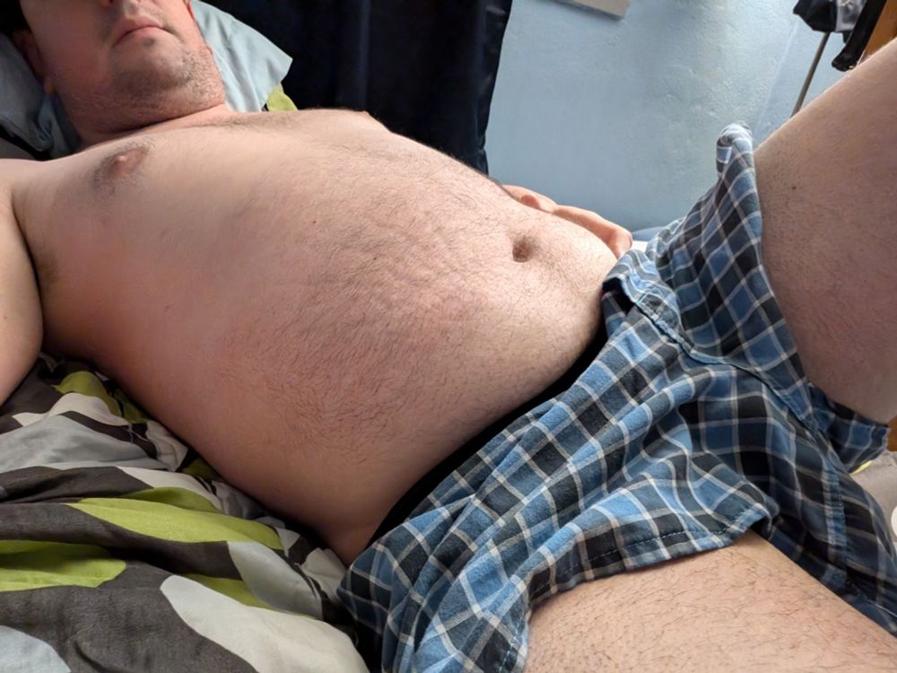 Adult man laying in bed in underwear, showing his belly