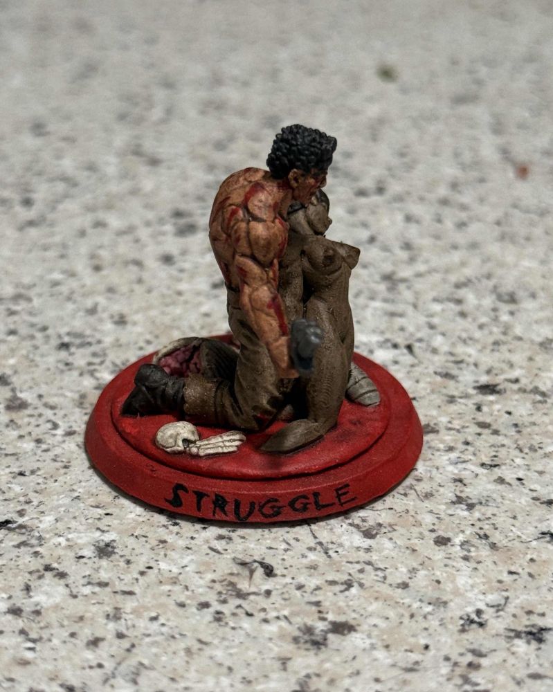 A side view of the Berserk mini, showing off Guts' and Casca's profiles, as well as the word "Struggle".