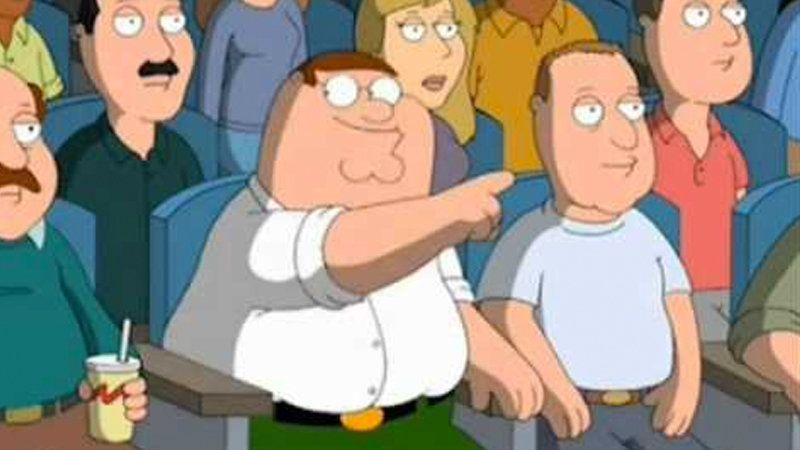 Peter Griffin from Family Guy sits in a movie theater, smiling with recognition and pointing at the screen. He is not speaking but is glancing at fellow audience members excitedly.