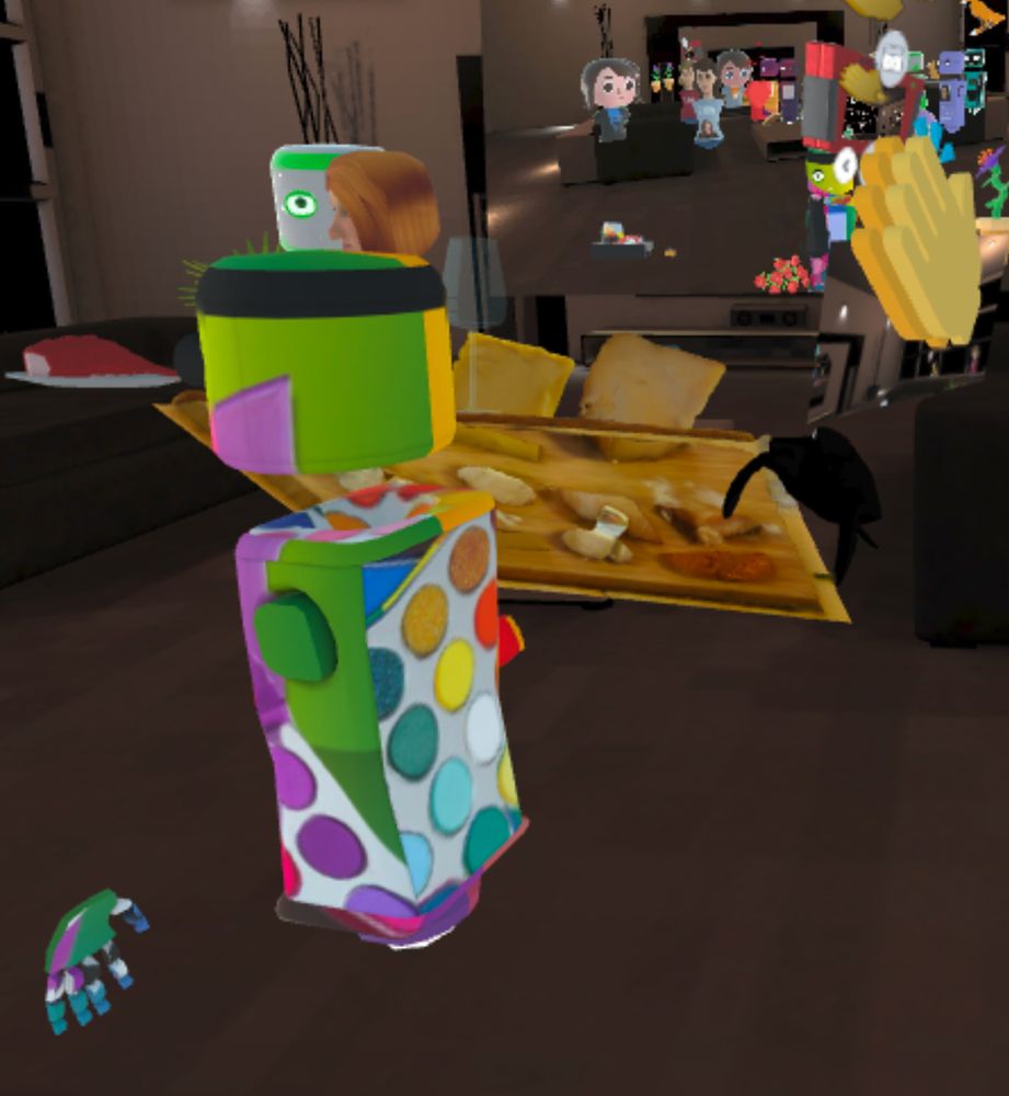 Screenshot from Mozilla Hubs. An avatar in the foreground is donned with colors of the rainbow. Snacks clutter the background. 