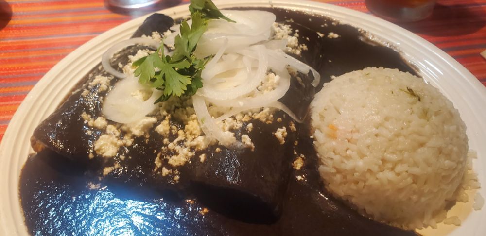 a plate of enchiladas smothered in black mole sauce, with cotija cheese, onion and cilantro and a perfect scoop of white rice