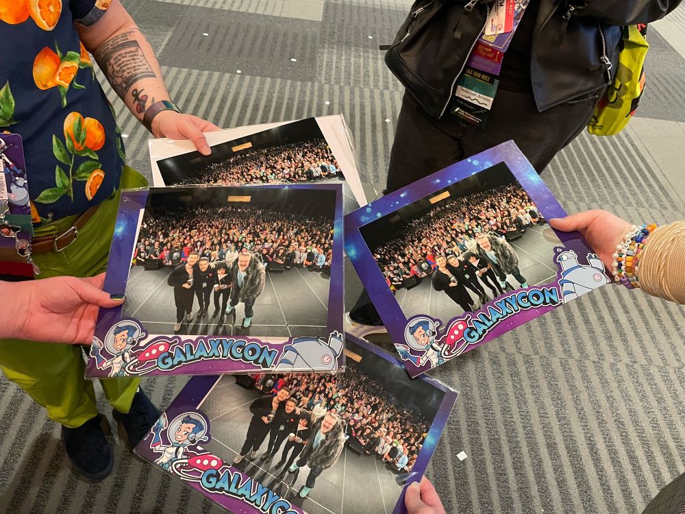 A POV shot of 4 people holding 4 copies of the Our Flag Means Death panel photo from GalaxyCon Columbus.