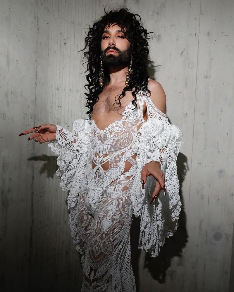 Conchita Wurst posing in a white knitted-like dress
