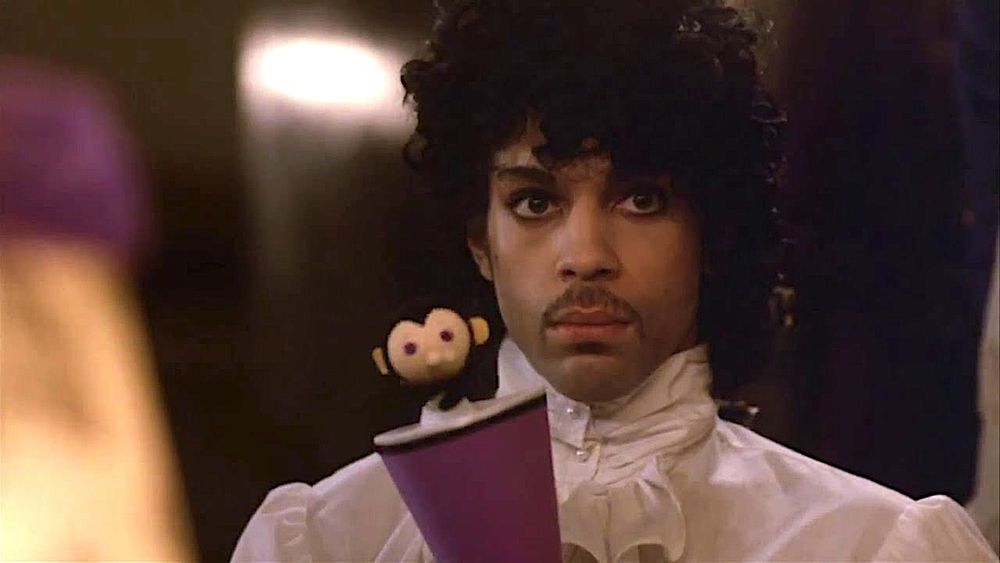 The musician Prince, dressed in a very puffy blouse, performs cruel ventriloquism with a weird little puppet toy in his movie "Purple Rain".