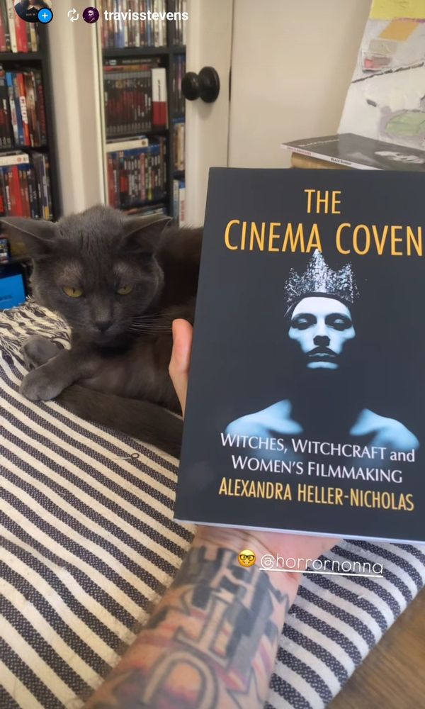 A beautiful black cat sits next to my book THE CINEMA COVEN: WITCHES WITCHCRAFT AND WOMENS FILMMAKING, held by Travis's tattooed arm, with Martyn Conterio's book on Mario Bava's Black Sunday in the background