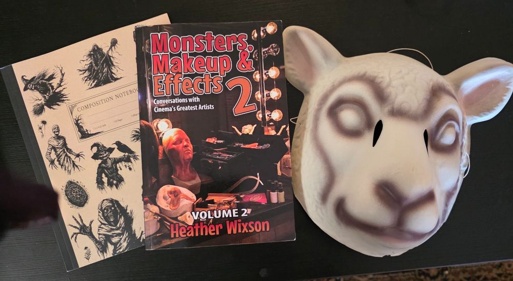A notebook with vintage Halloween motifs, Heather Wixson's book Monsters Makeup And Effects v2 (signed!) and an official replica of the lamb mask from Adam Wingard's You're Next