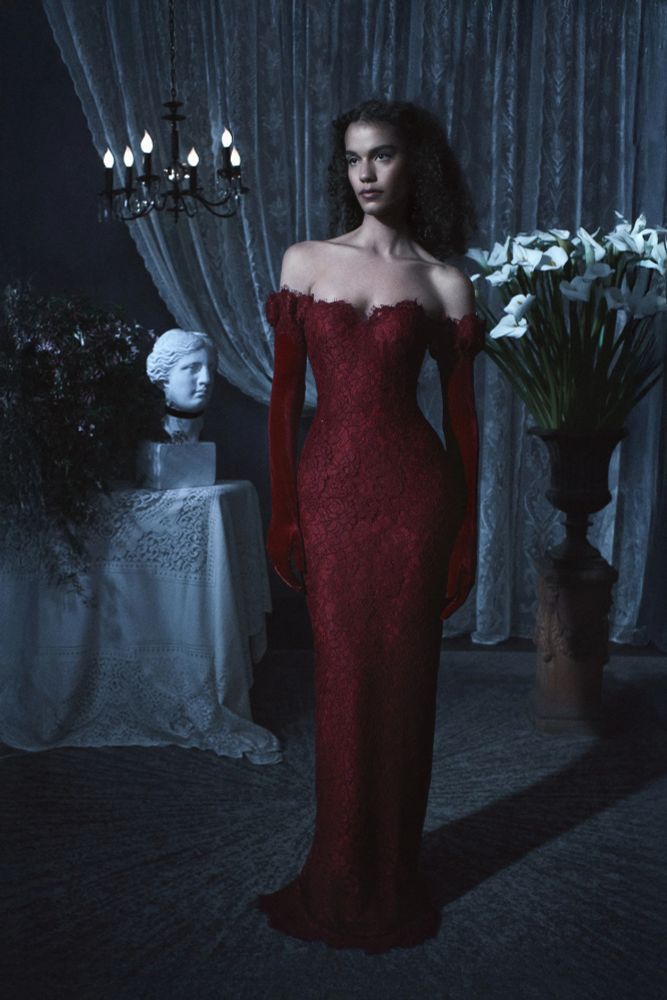 Look 7 of 16 of Rodarte's Fall 2025 RTW Collection, designed by the Mulleavy sisters, model Shelby Hayes wears a blood-red, form-fitting gown that puddles to the floor. The gown has a lace pattern on it, and a heart-shaped bodice. She wears shoulder-length gloves of red velvet.  