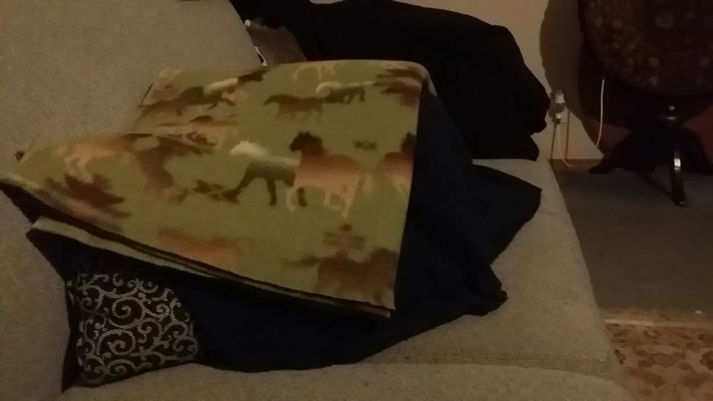 Photo is a close-up view of a light blue couch from the side. In the center is a pile of folded blankets draped over a small pile of pillows