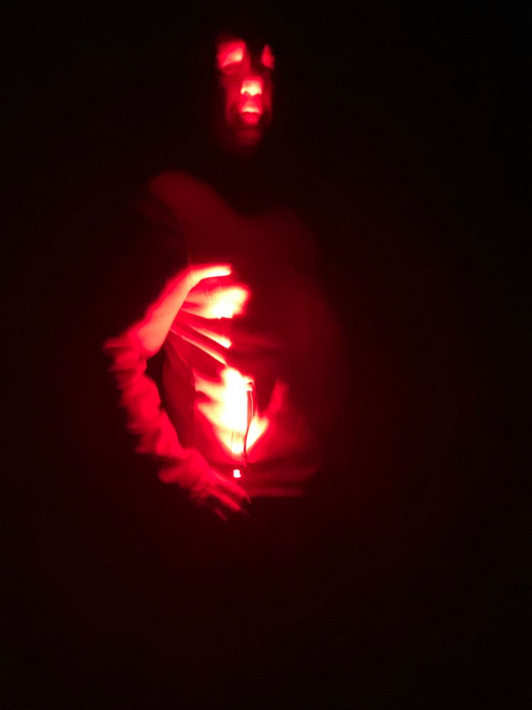 A man shines a kiwi-friendly red torch on his face in the dark.