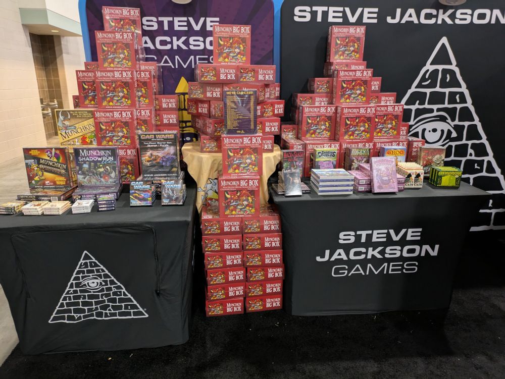 Two tables full of boxes of board games at the Steve Jackson Games GenCon booth.