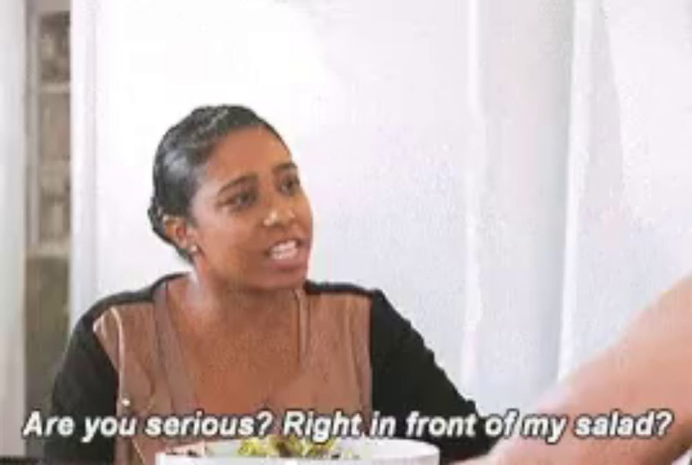 a woman is sitting at a table talking to another woman while holding a salad .