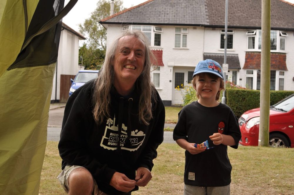 A smiling adult male kneeling down next to a smiling child. There is an obvious familial similarity between them 
