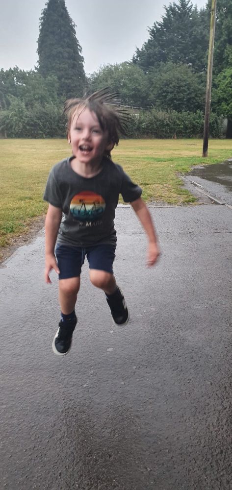 A smiling, drenched child leaping in the air 