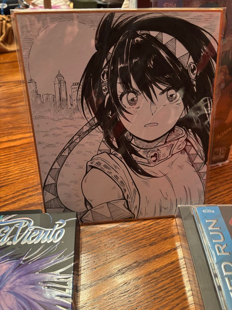 A black and white shikishi drawing of Annet Mayer/Myer looking determined with a city in the background. It sits on a wooden table.