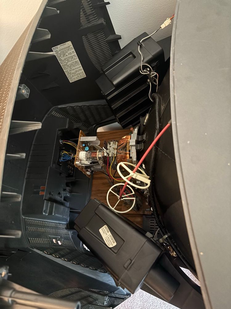 A timid shot of the internals of a Sony KV-27V42 tube television, featuring large speakers, an RGB-SCART mod, and a jungle of cables and circuitry that I don’t even close to understand.