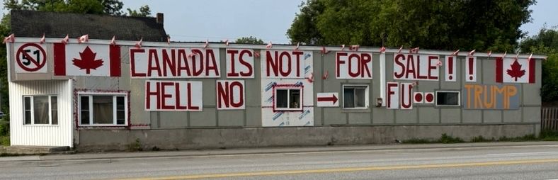 Sign on side of building. 51 with a red slash through it. The Canadian flag. Text reading Canada is not for sale. Hell no. FU Trump.