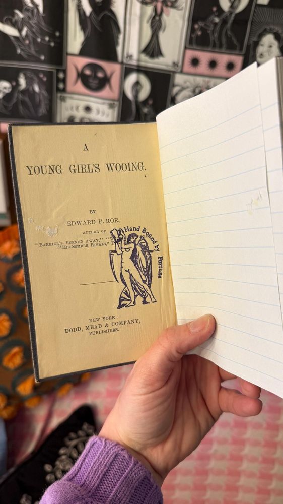 inside view of the hand-bound journal. the inside cover is retained with the title "A Young Girl's Wooing" by E.P. Roe, and a stamp that reads "Hand Bound by Fortuna." the journal's lined page is on the opposite side.