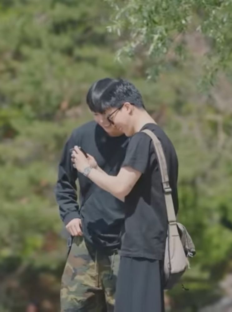 Jikook smiling with their heads together as jimin shows jk something on his phone.