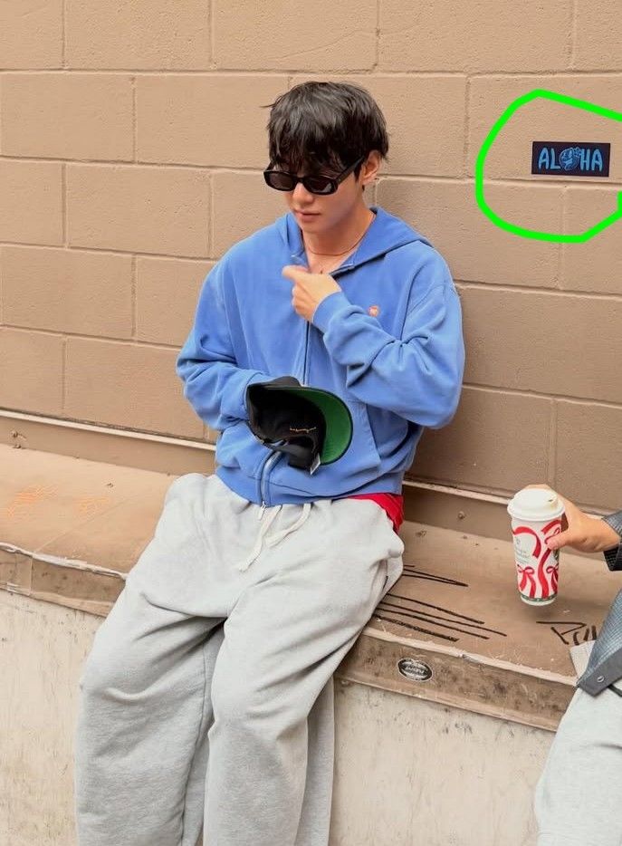 Tae from his insta, looking like the cosiest omega to ever omega in a soft blue hoodie and grey sweat pants. A sign/sticker on the wall next to him says "Alpha."