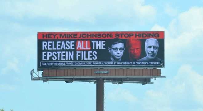 A photo of a billboard near Mike Johnson’s office in Louisiana that reads “HEY, MIKE JOHNSON: STOP HIDING/RELEASE ALL THE EPSTEIN FILES” alongside images of Jeffrey Epstein, Trump, and Johnson.