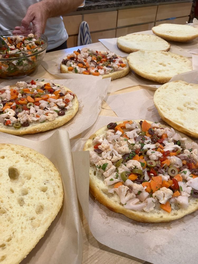 Multiple round loaves of semolina bread topped with olive salad, ready for the meat and cheese layers