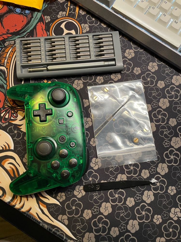 A green Switch Pro controller with a replacement stock trigger/bumper ribbon cable next to some tools.