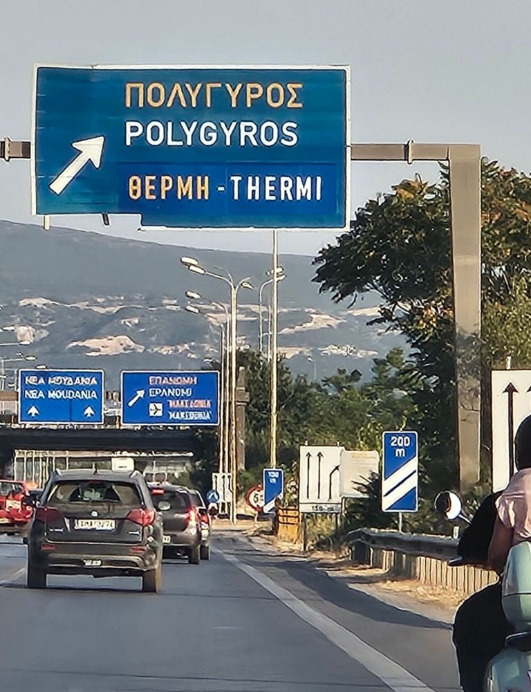 Foto von griechischer Straße, Ortschild weist in eine Stadt Namens Polygyros. 