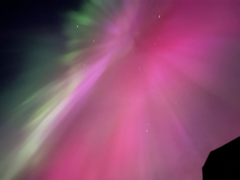 A picture of the Aurora borealis over head at night. A bright pink sky with some green, yellow and blues. 