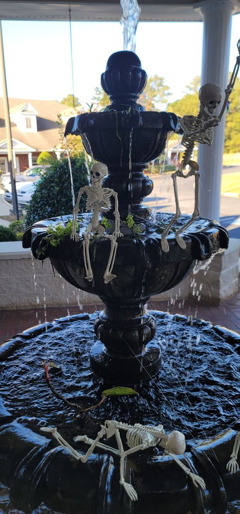 One small skeleton sitting on the middle their as another skeleton looks like it's diving into the base of the fountain