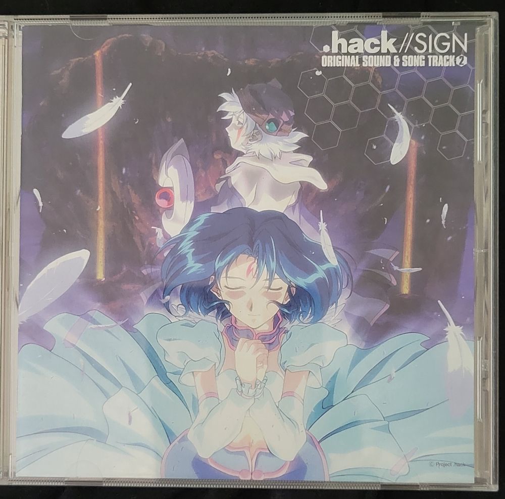 The second soundtrack for the og .Hack//Sign anime on cd! Music composed by the legendary Yuki Kajiura, and featuring the main characters Tsubasa and Subaru on the cover art. Subaru is at the forefront wearing her sky blue dress. She is pale with short midnight blue hair and a red stylized lightning bolt-like tattoo on her forehead. She is closing her eyes and clasping her hands in prayer while surrounded by white feathers. Behind her is Tsubasa with their back to the viewer and looking back at Subaru. They're wearing a reddish-brown cap and a simple-looking tan robe with a white mantle. They are pale with messy short white hair and a red stripe tattoo'd going down from their eye to their cheek. They're holding a silver cane with a red orb suspended within the C-shaped cap. Behind both of them is a cliff jutting upwards into the sky, with a hexagonal grid pattern partially obstructing the top right where the logo is.