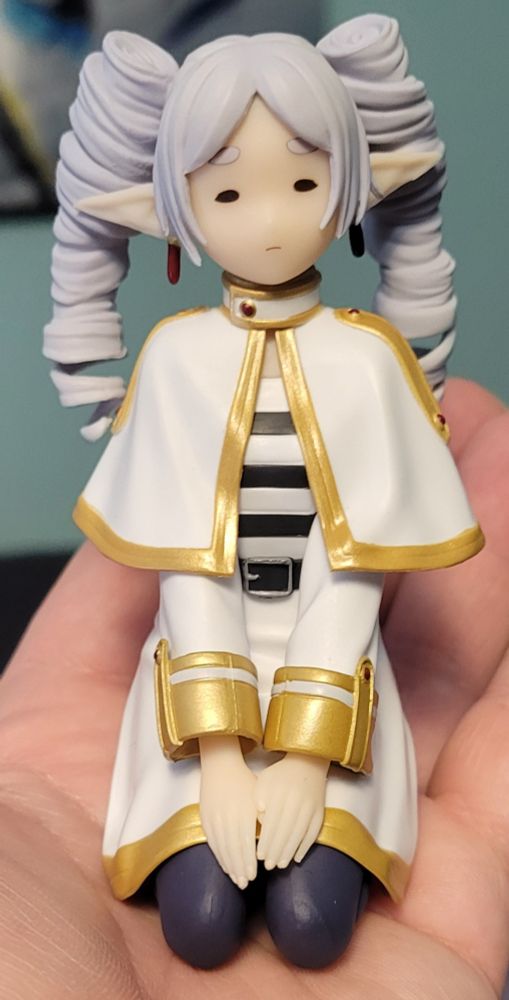 A small figurine of Freiren the elf sitting on her knees and looking like she just rolled out of bed late and got chastised for it.