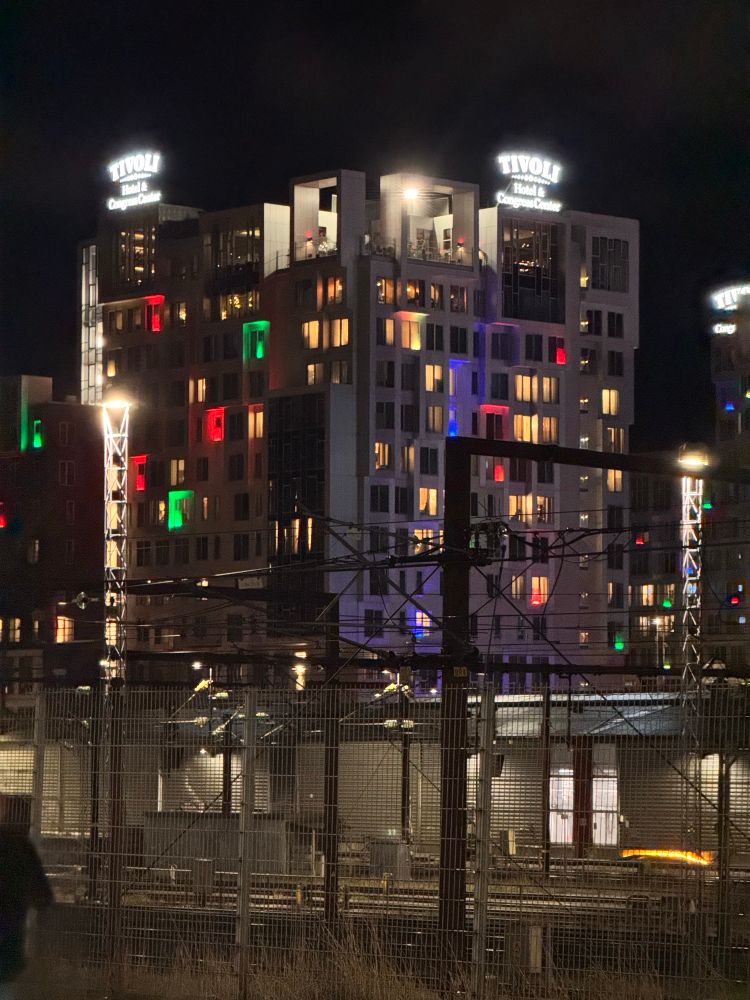 Hotel seen across railway tracks, colourful lights in many of its windows