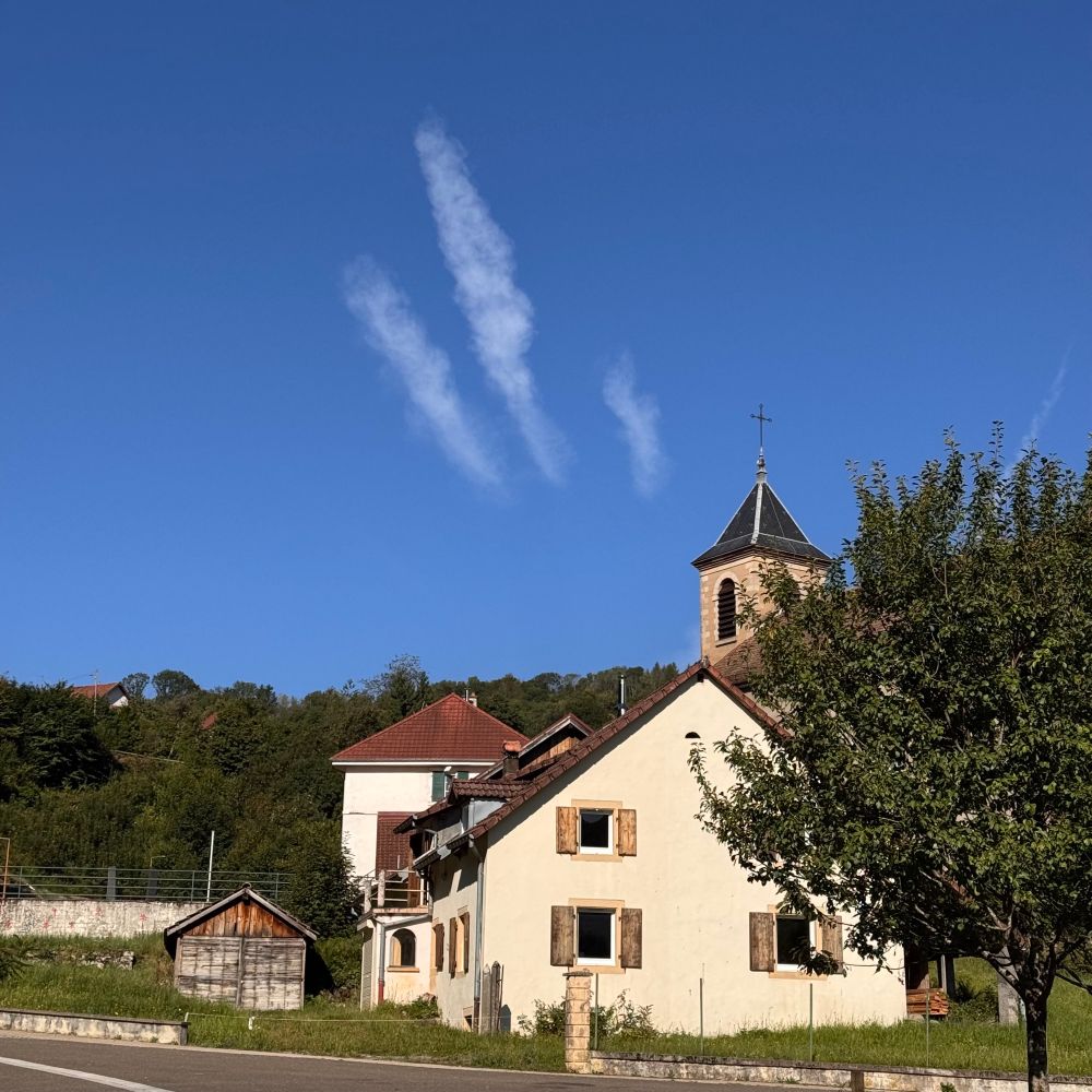 Three clouds in a blue sky, like III, above a village
