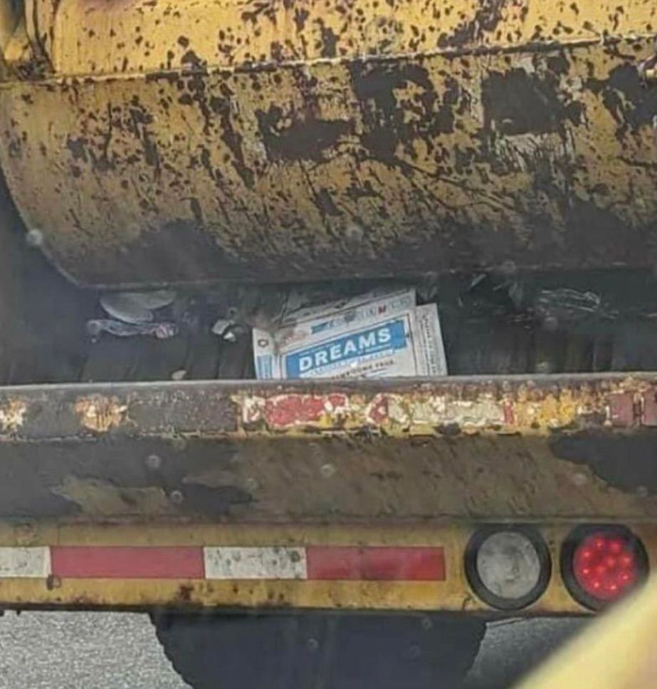 Paper reads “dreams” shoved in back of garbage truck