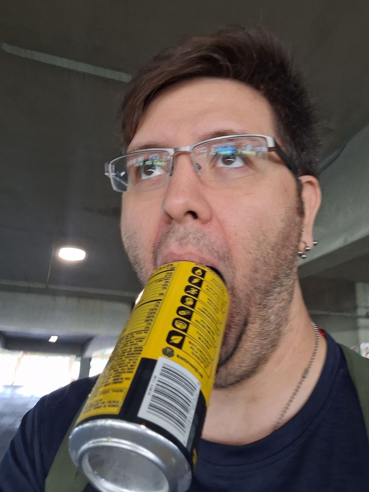 a man with glasses walking in a parking garage with a whole Monster energy can in his mouth