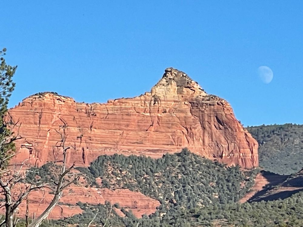 Nearly full moon to the right of a redrock ridge.