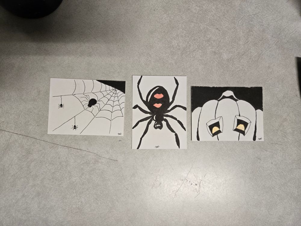 Three cards in black ink with slight metallic highlights. The first is a spider web with a few spiders. Second is a large black widow spider. Third is a jack-o-lantern.