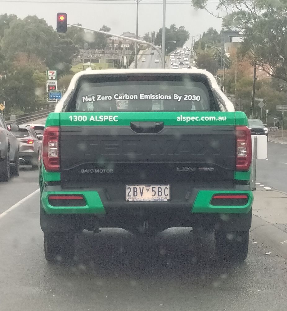 Big black and green ute. Has an exhaust so not electric. On the back window in big white letters it says 'Net Zero Carbon Emissions By 2030'