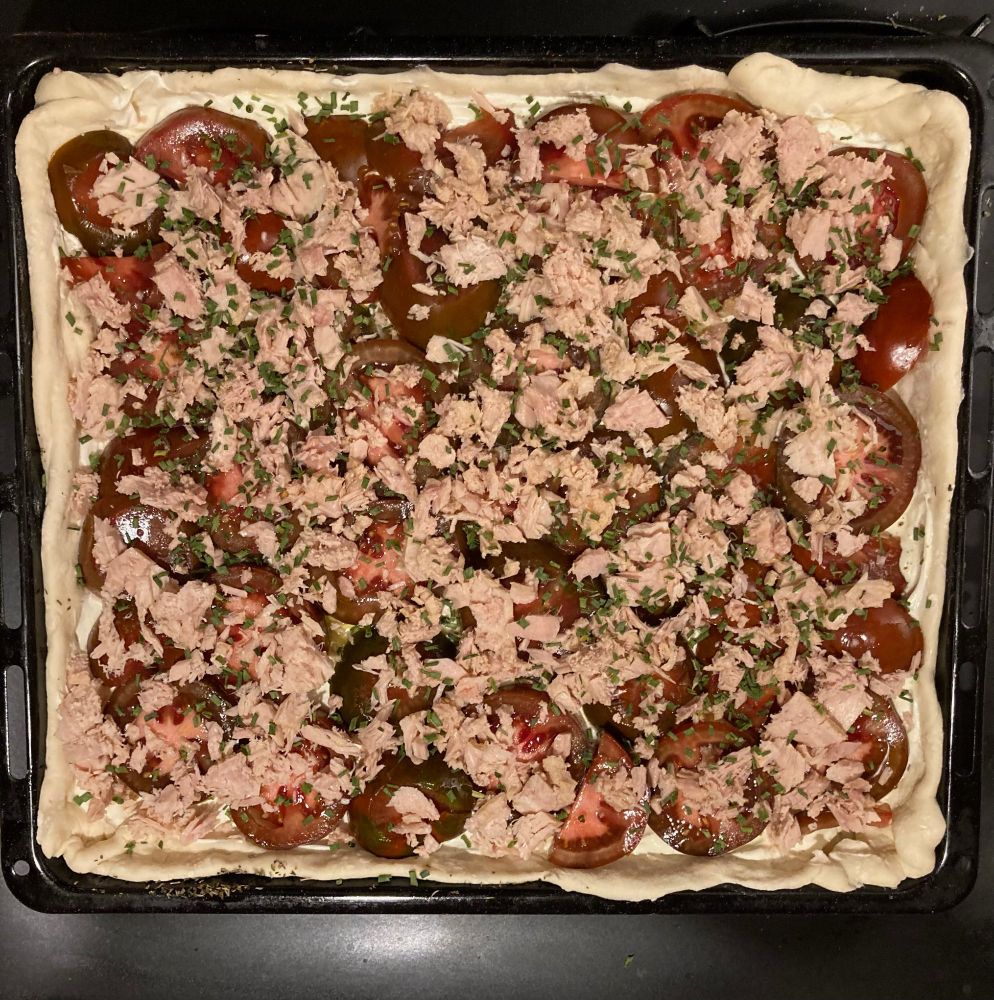 Pizza avant cuisson : pâte maison posée sur une plaque huilée d'olive avec des herbes de Provence, fond crème fraîche salée poivrée sauvagement depuis la Réunion, rondelles de 7 tomates kumato légèrement salées, émietté de thon cibouletté ostensiblement.