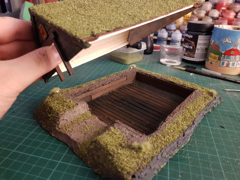 The roof lifted. The inside is made of darkened wood, in a shallow barrow in the earth. Could be homey, but it's empty and abandoned.