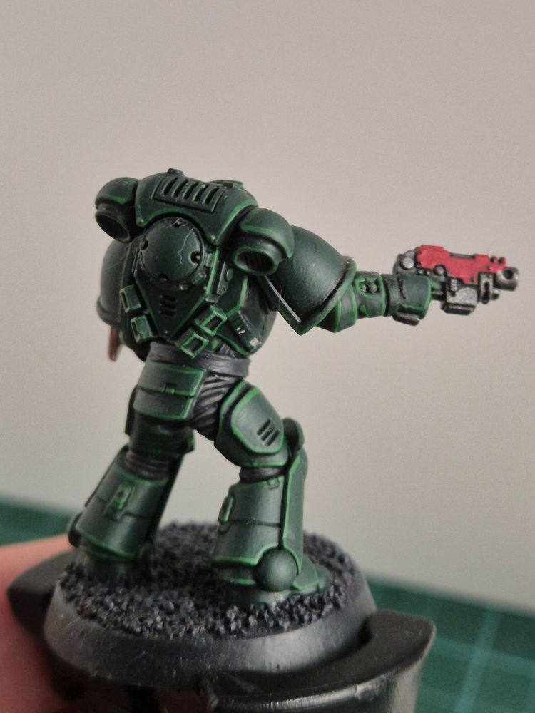 The same marine, from the side. We can't see his damaged arm, but his bolt pistol is shown prominently, aimed at something. Maybe a tyranid that tries to scoop some fleshy marine arm out of a power armour cone.