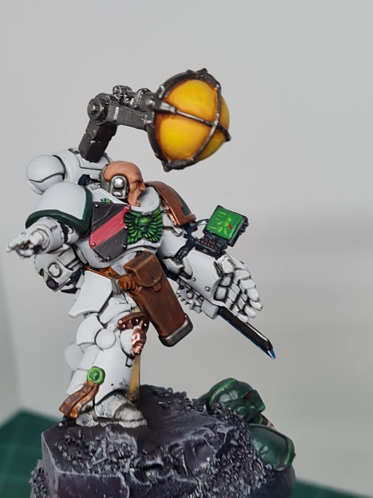 A space marine apothecarius, heavily kitbashed. On his heavy powerfist, riddled with medical equipment like an energy scalpel, is a screen attached. Someone in his squad has an arm-related emergency as we can see on the screen. Who knows who this could be~