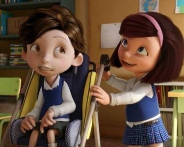 Fotograma del corto "Cuerdas" con Nico en una silla de ruedas y su amiga al lado. Están en clase y llevan uniformes del cole con camisa blanca. Chaleco azul y él pantalón corto gris y ella falda azul a cuadros. 