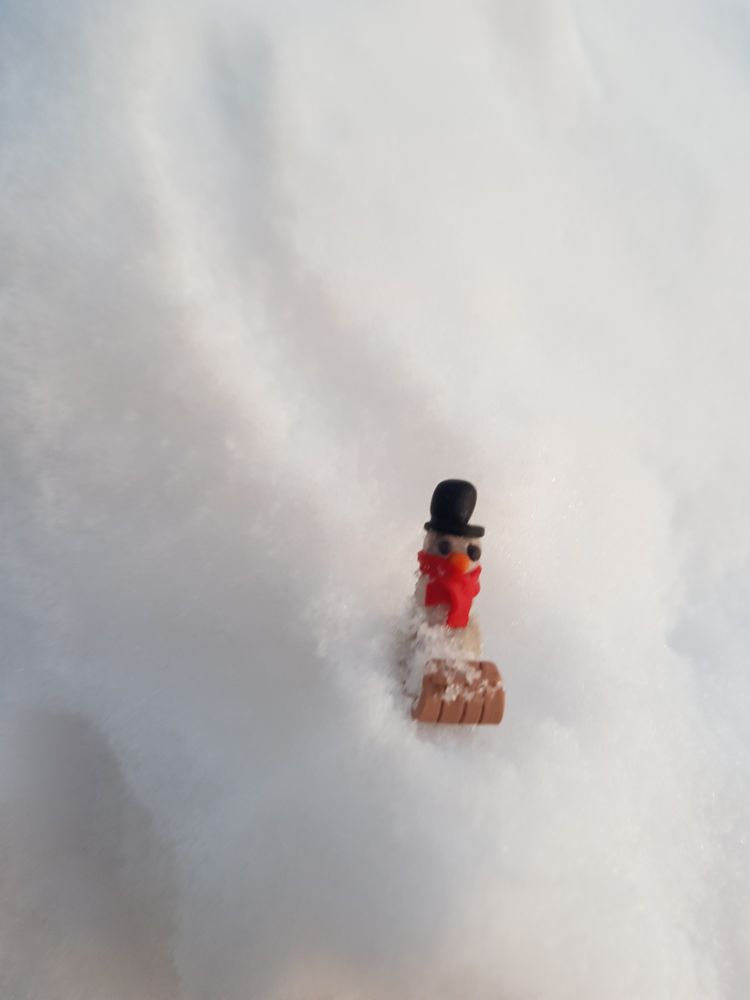 A miniature snowperson going down a snowy hill.