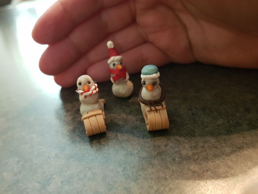 Three tiny snowpeople on luges.