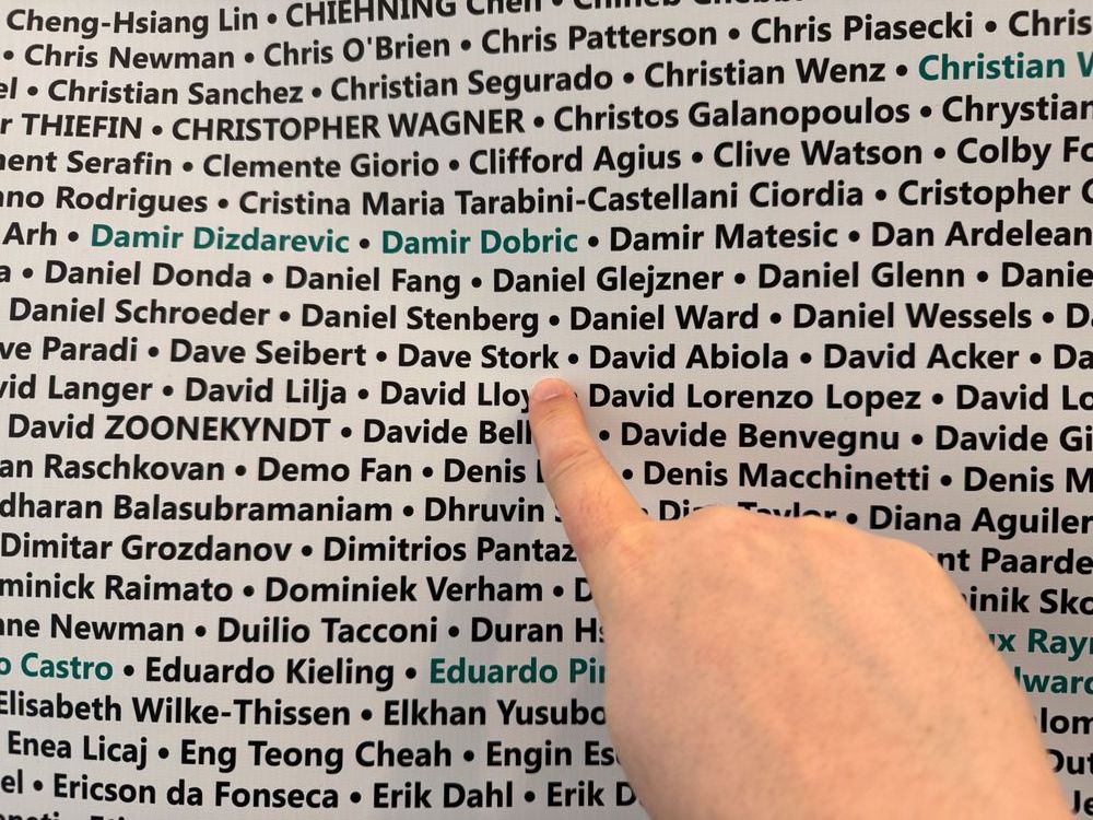 Zoomed in MVP All Names Banner. A hand gestures towards the name "Dave Stork," highlighted in teal on a list of names written in black text. The finger emphasizing its significance among the other names in the list.