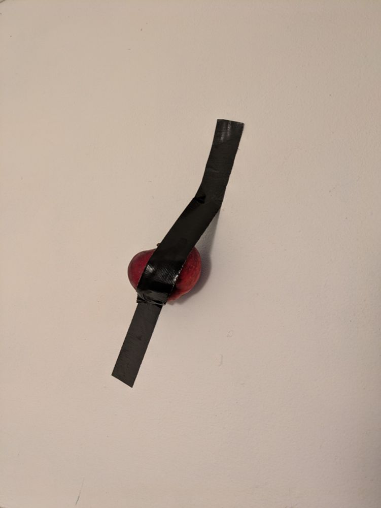 A red apple duct taped to a white wall.