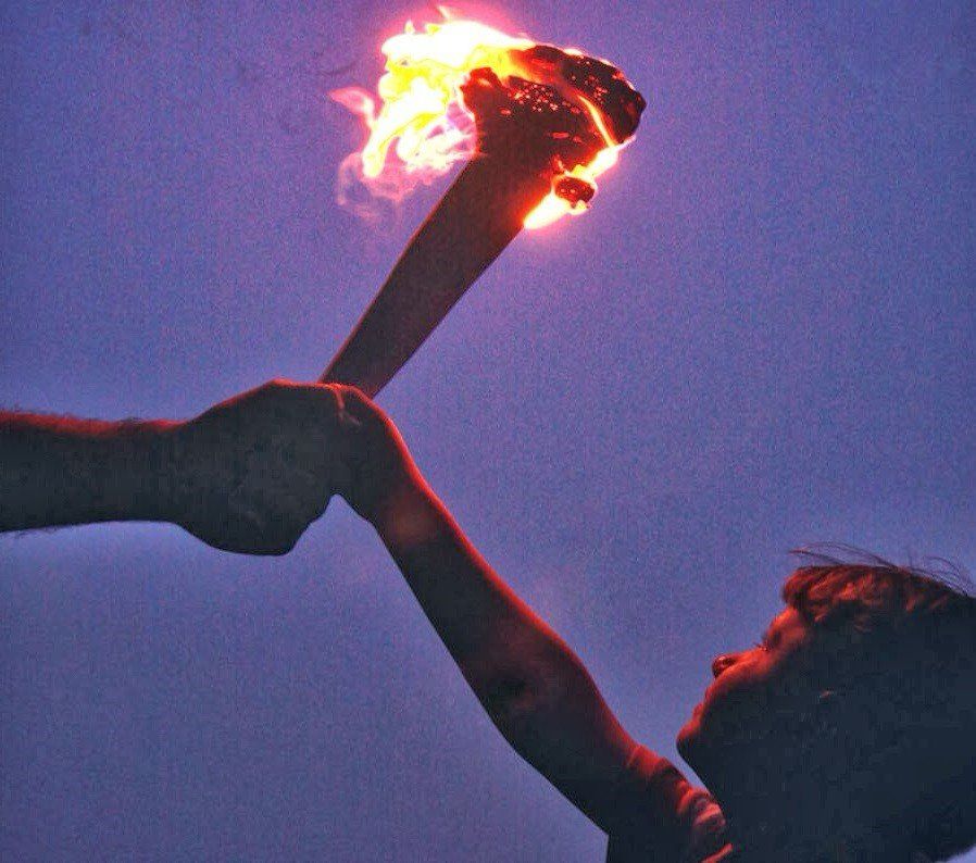A hand holding a torch is passing it to a child looking up